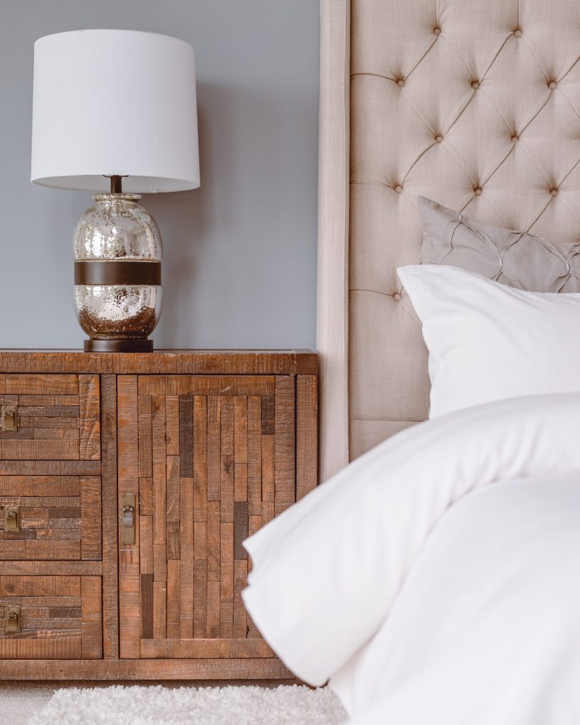 Cozy bed with white linens, wooden side table and a lamp 