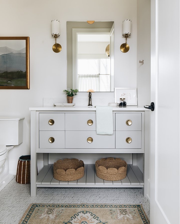 Light colored bathroom with brass handles and wicker baskets under the sink 