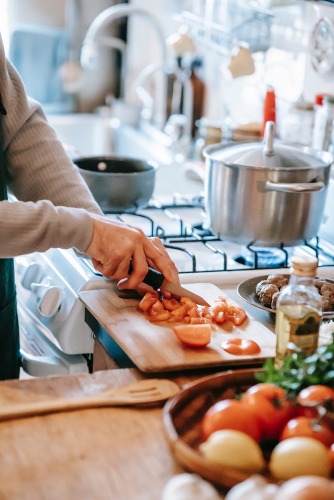 Someone chopping tomatoes and using a pot to cook