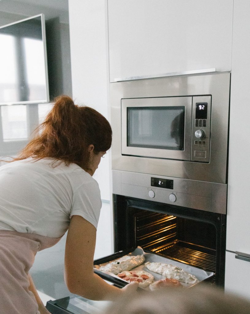 A lady putting dough inside the baking oven 