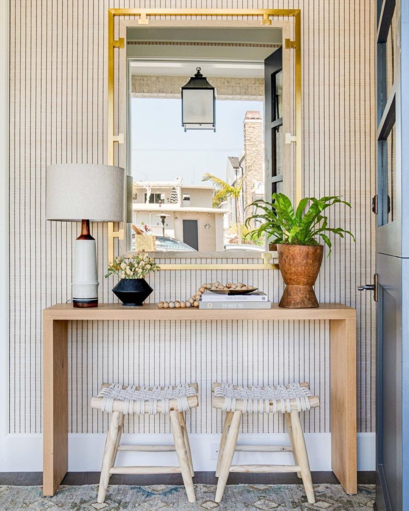 An entryway or foyer with a rectangular mirror, plus console table with a lamp and other accessories. 