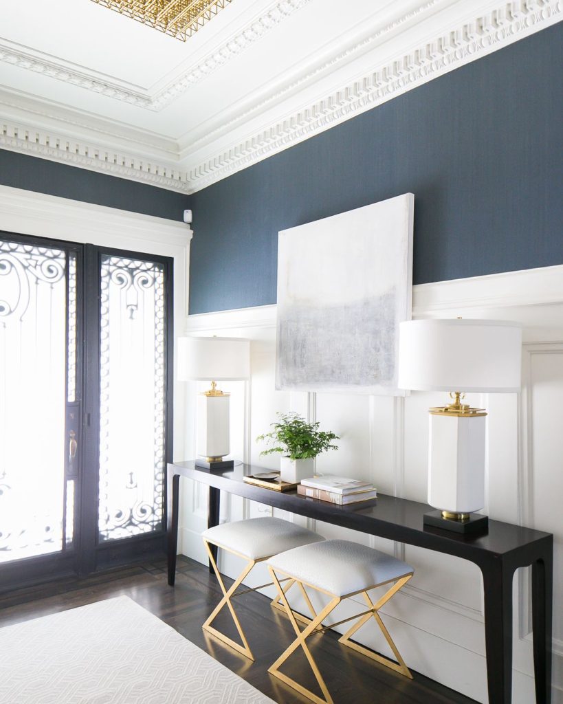 Gray and white entryway with intricate detailing of wood paneling on a wall and crown molding. 