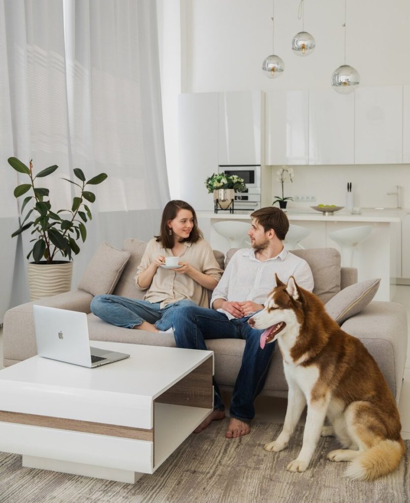 A lady, man, and dog in the white living room sofa. 