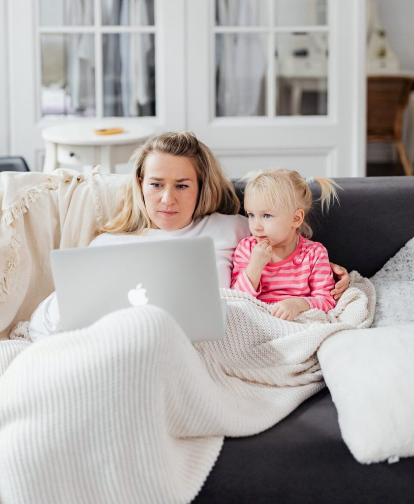 Mom and daughter looking at the laptop while sitting in the gray sofa.