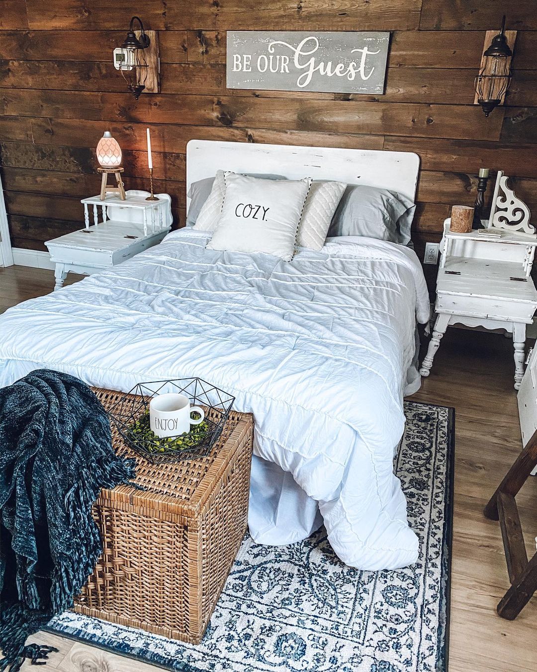 Farmhouse Bedroom with wooden walls, white bed, wicker trunk and blue throw 